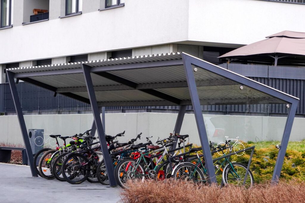 Fahrradgarage mit moderner Ueberdachung vor einem Mehrfamilienhaus mit mehreren abgestellten Raedern