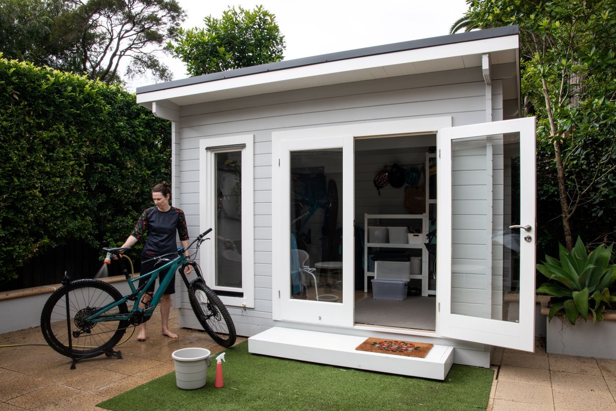Fahrradgarage im Garten mit geoeffneter Tuere und Person beim Reinigen eines Mountainbikes