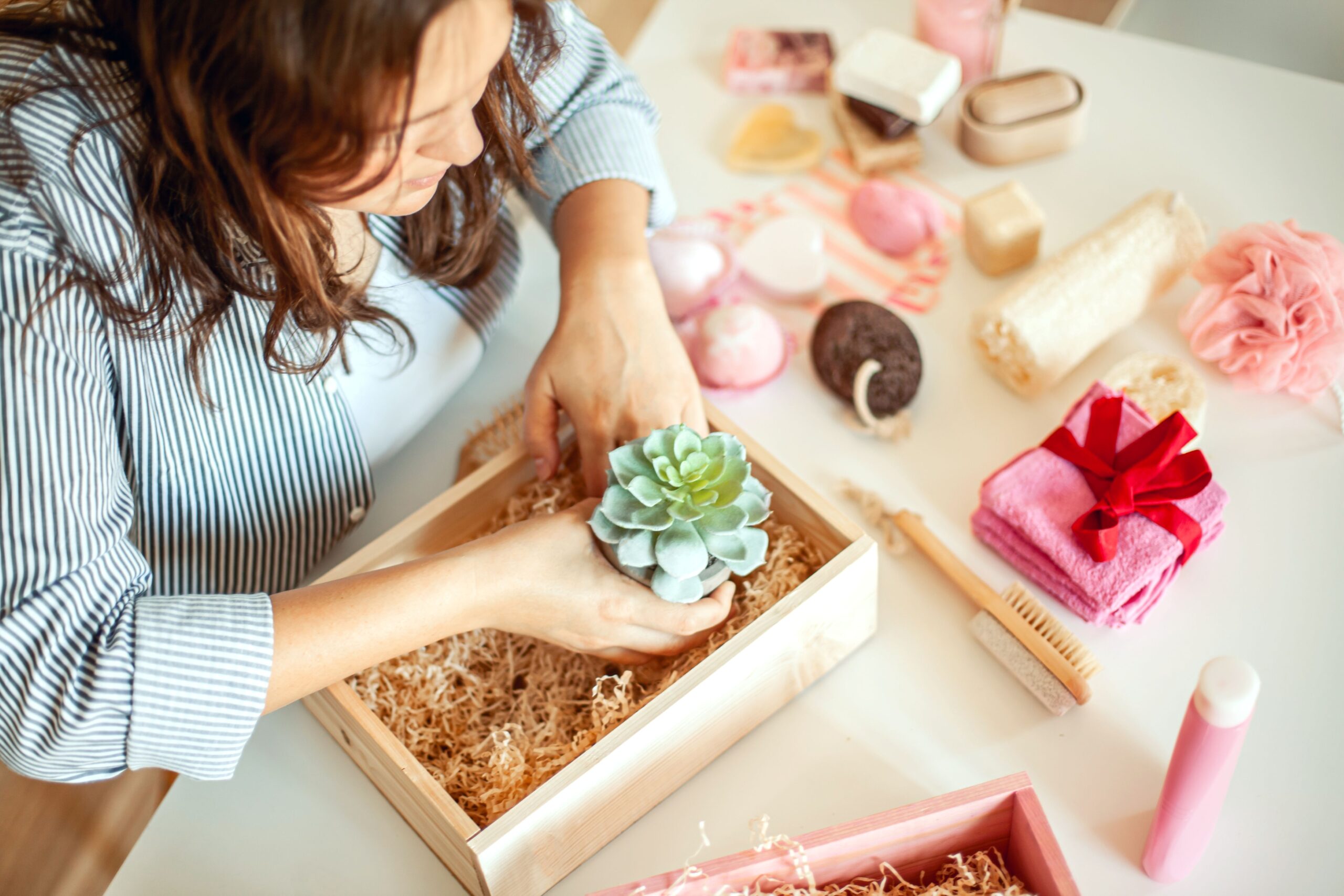 Frau stellt liebevoll Geschenkbox mit Pflegeprodukten und Pflanze zusammen – Auswahl hochwertiger Elemente für individuelle Präsentkörbe