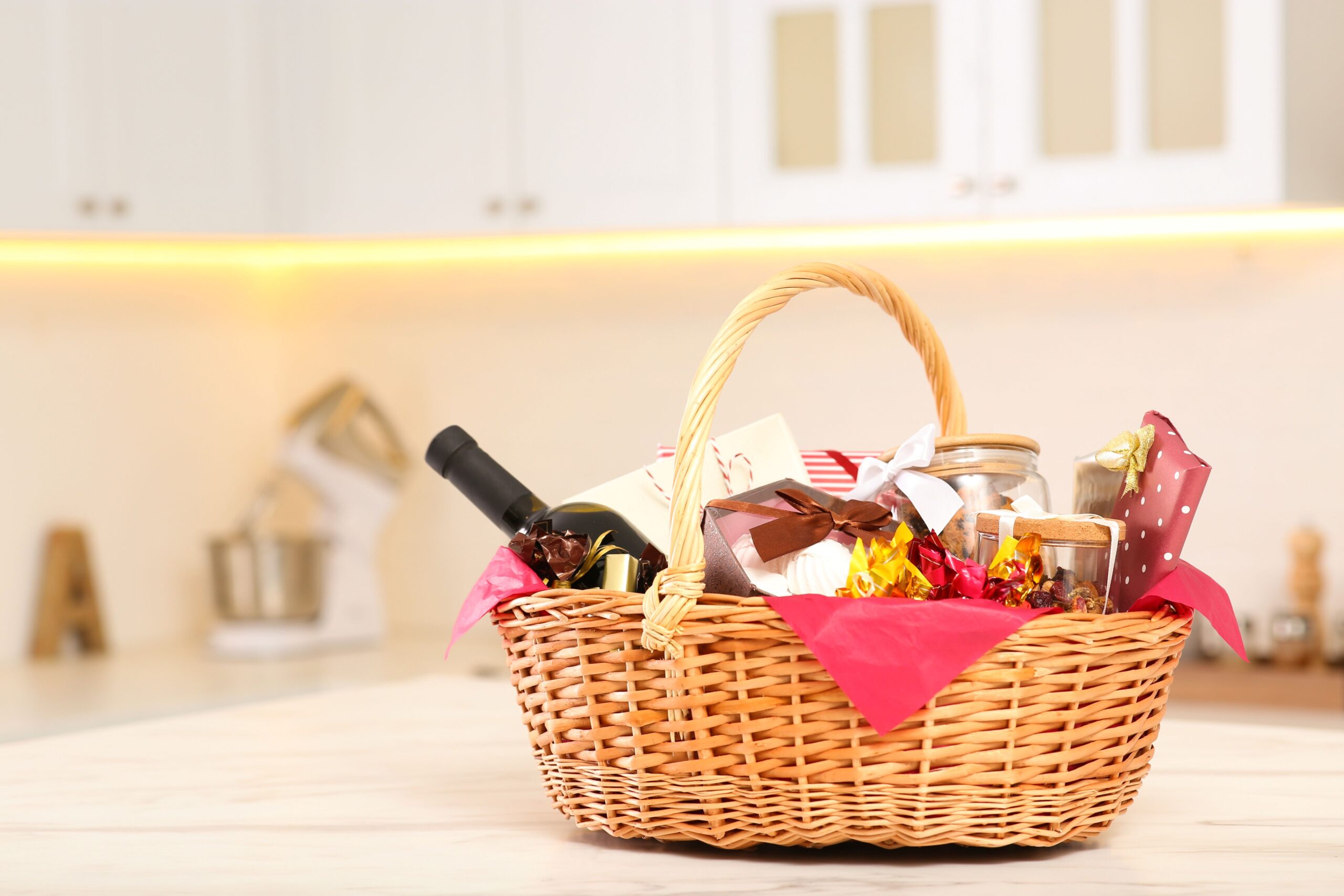 Stilvoll gefüllter Präsentkorb mit Wein, Konfekt und Karte auf hellem Küchentisch